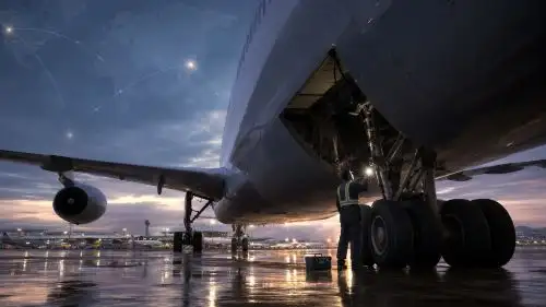 東京発航空機の車輪格納部から遺体発見死後72時間と候補機9M-XBFの運航履歴アイキャッチ画像 - clairvoyant report Wide view of a large aircraft on a wet tarmac at sunset, ground crew inspecting the landing gear under the wing.